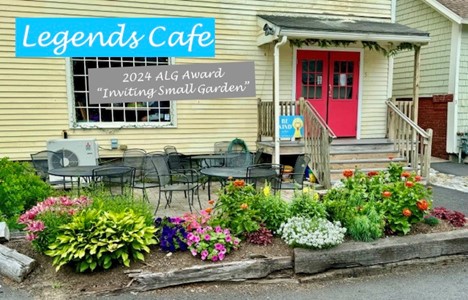 A bright flower garden in front of the Legend Cafe entrance. Tables and chairs are on the patio in the background.