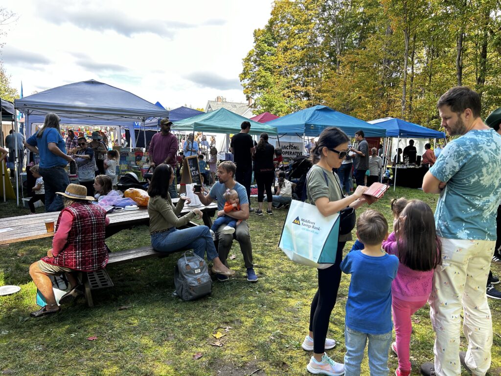 Kids and adults are seated at picnic tables and standing around discussing the next step. In the background, the tents are very popular.