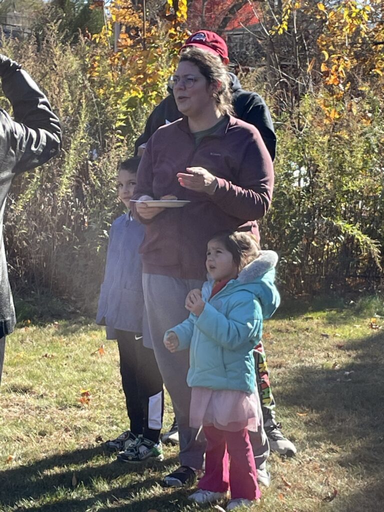 A woman holding a slice of pie stands with her two kids in the sunlight.