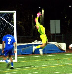 A young man in bright yellow gear leaps into the air with his hands above his head. the goalpost is in the background.