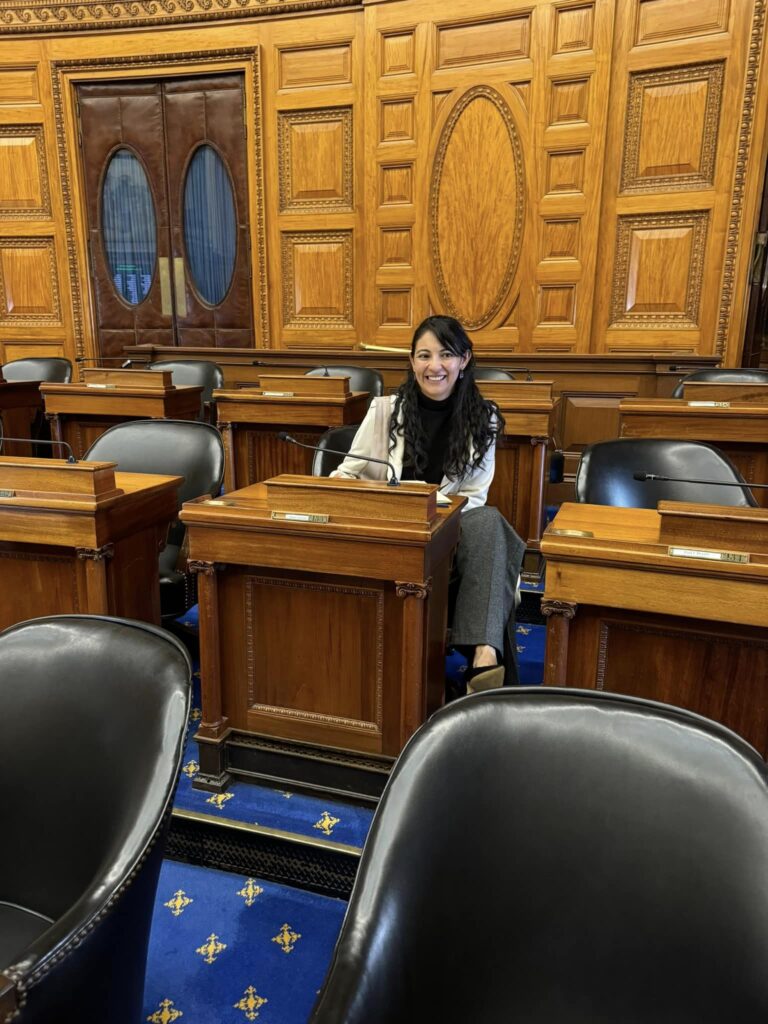 A woman sits at a small wooden desk, in a wood-paneled room. there are many other desks in the picture.