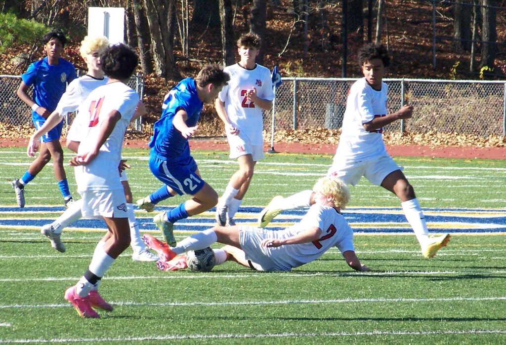 A North Andover player is on his back on the ground. An AB player seems to be jumping over him to avoid disaster.