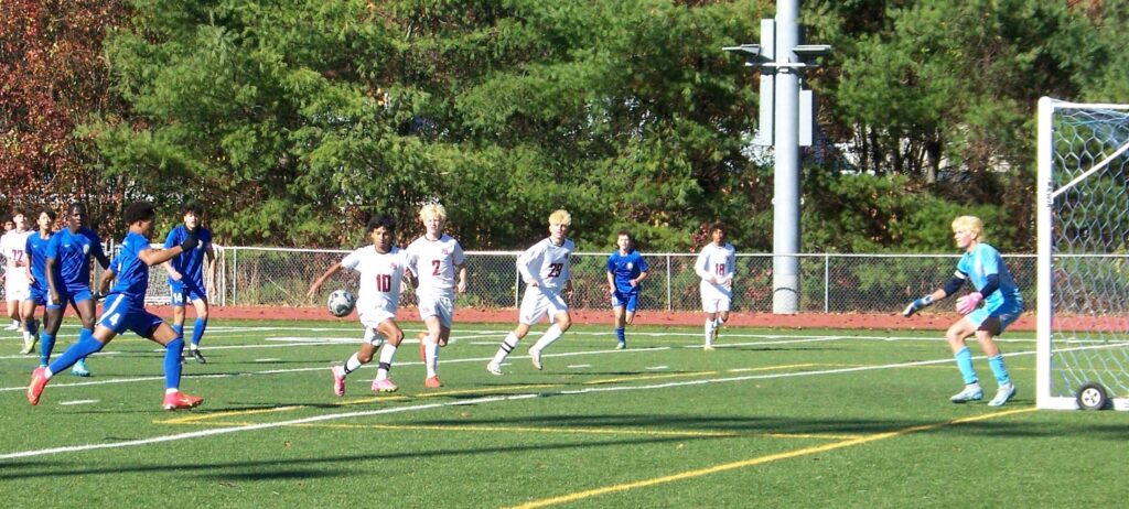 A group of young men race towards the soccer goalposts. One AB player is heading to intercept the ball.