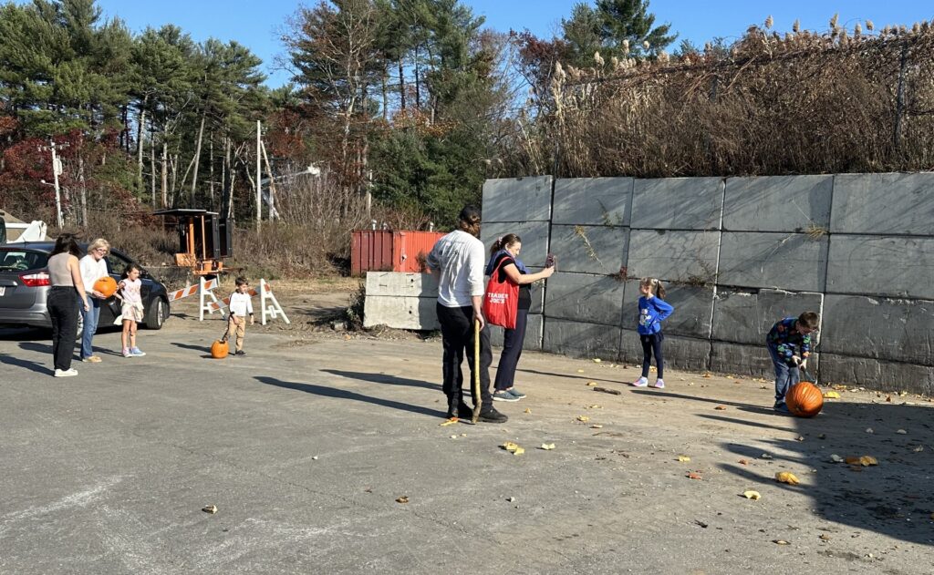 Kids and adults mill around. One kid is working on a large pumpkin.