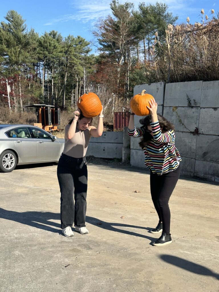 Two woment hold large pumpkins over their heads. They are getting ready to throw them on the ground for the pumpkin smash.