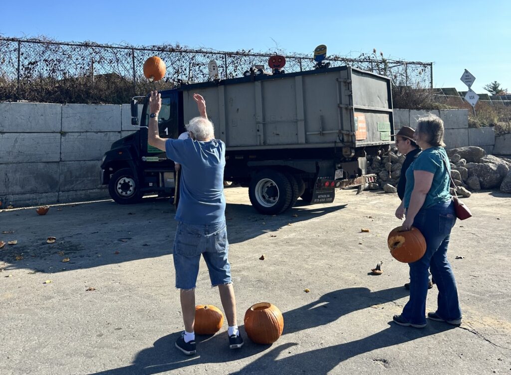 An older man tosses a pumpkin. A few other people wait their turn.