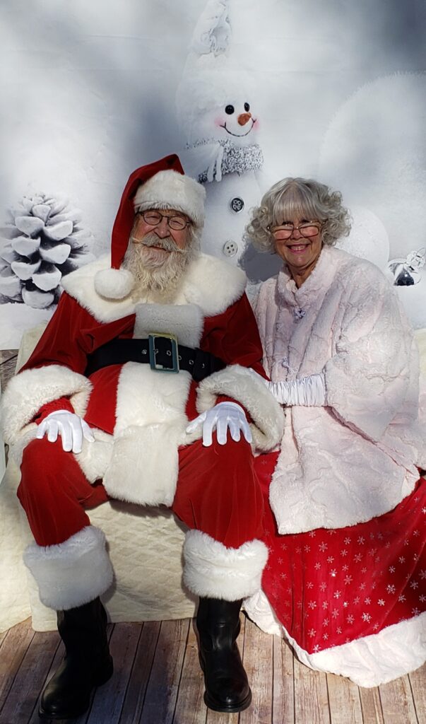 A man and woman dressed as Santa and Mrs Claus sit in front of a winter wonderland. Santa sports a truly wonderful beard (his own!).