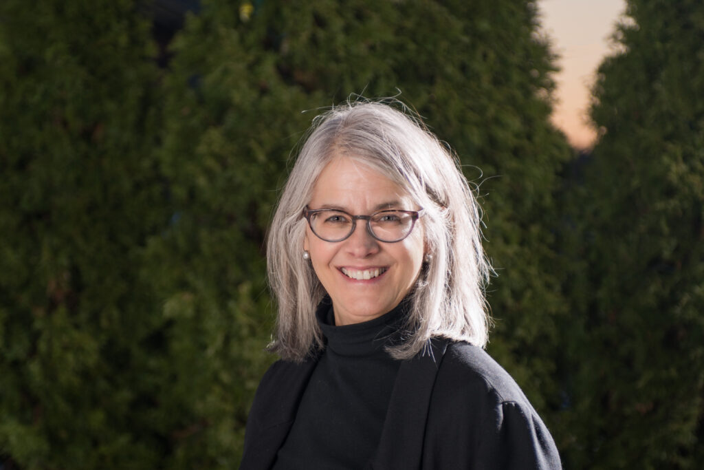 A smiling woman with shoulder length grey hair and glasses.