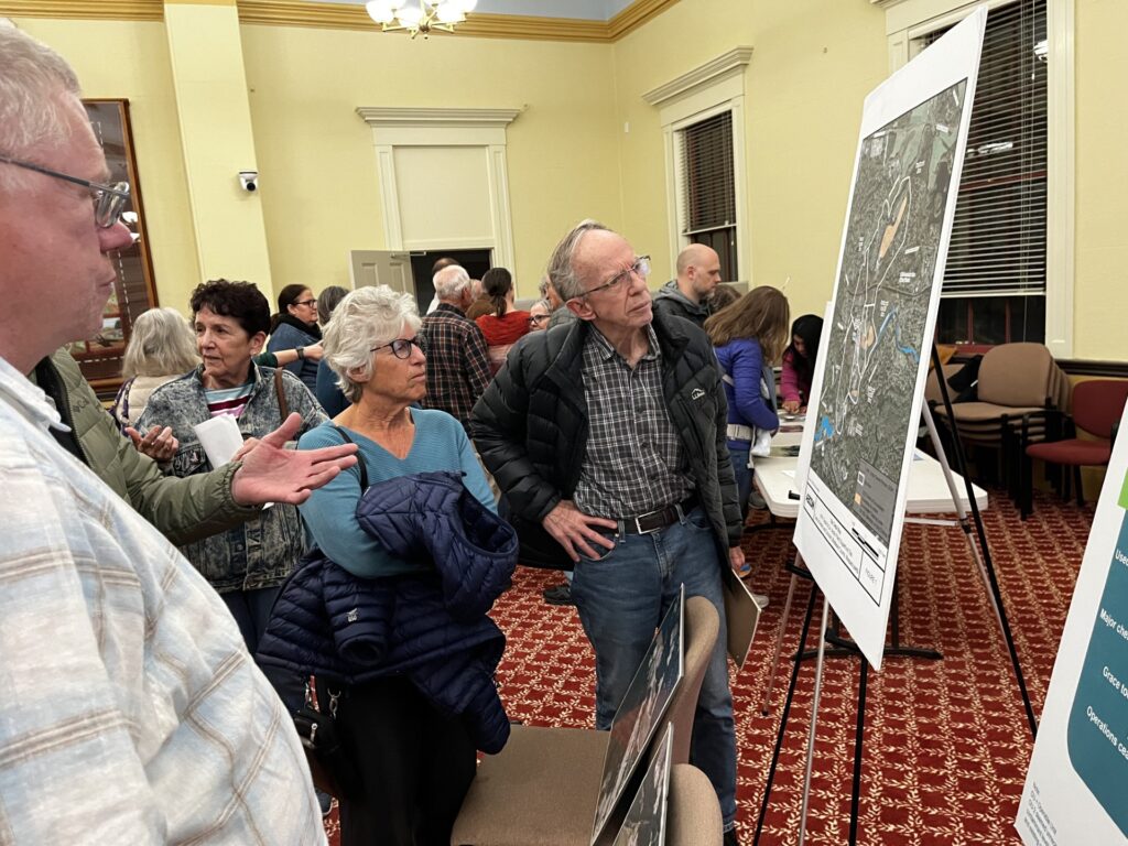 A group of people examine a poster in Room 204. There are also a number of people in the background.