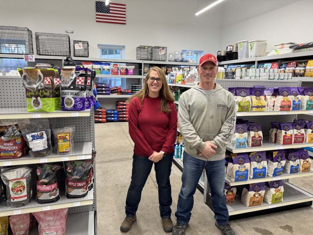 A woman and man, wearing work clothes, stand in the new well-stocked back room in a store.