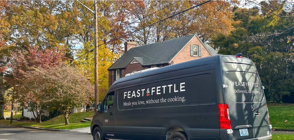 A grey truck with a Feast & Fettle logo is parked on a leafy neighborhood street.