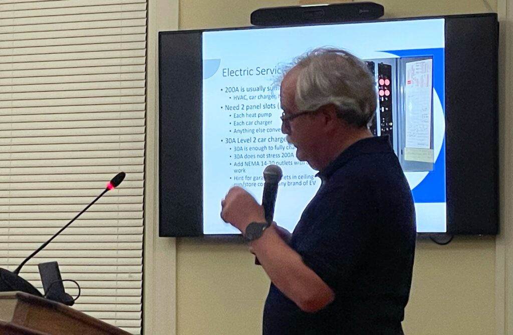 A different man stands at the podium. The screen behind him as information about electrical service for homes.