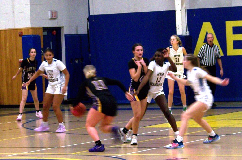 A girl wearing a black jersey (Bay Path) runs down the court dribbling a ball. Other girls, wearing white (AB) try to get in to block her and are in turn, blocked by Bay Path players.