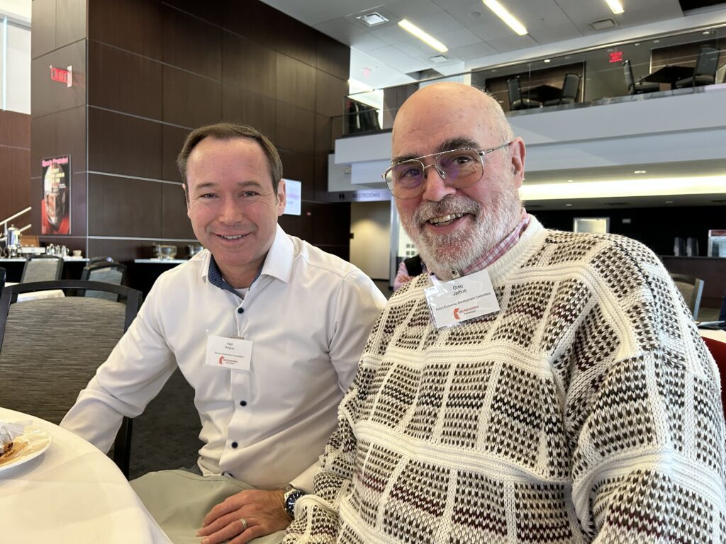 Two men sit at a table in a large room.