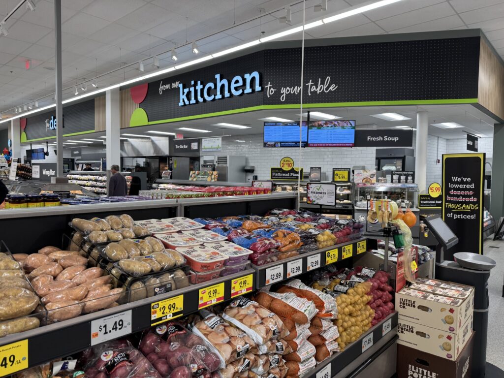 A view from the potato aisle. Potatoes of many types and colors are in the foreground, on the wall in the background, the sign reads, " From the kitchen to your table."