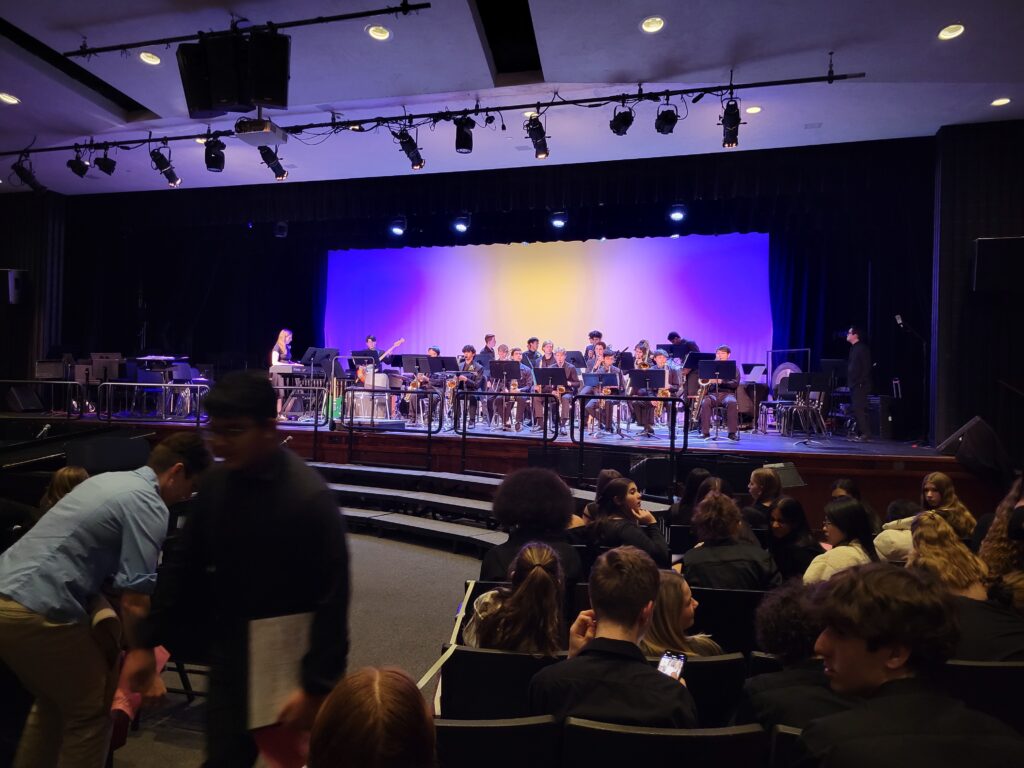 A band is up on a stage. In the foreground people are still getting seated.