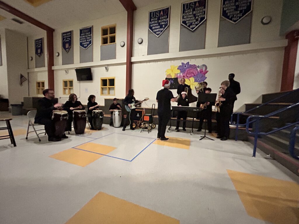 Four drummers a bass guitarist, and other musicians are playing music in the lower lobby by the auditorium.