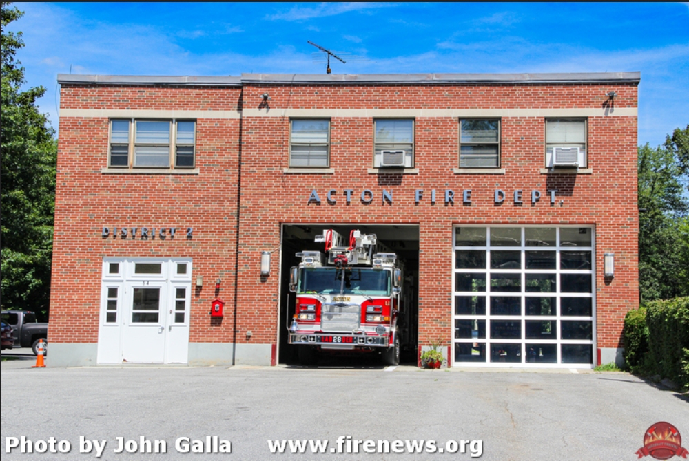 The South Acton fire station in the sun. One of the bay doors is open and a firetruck is in the entryway.