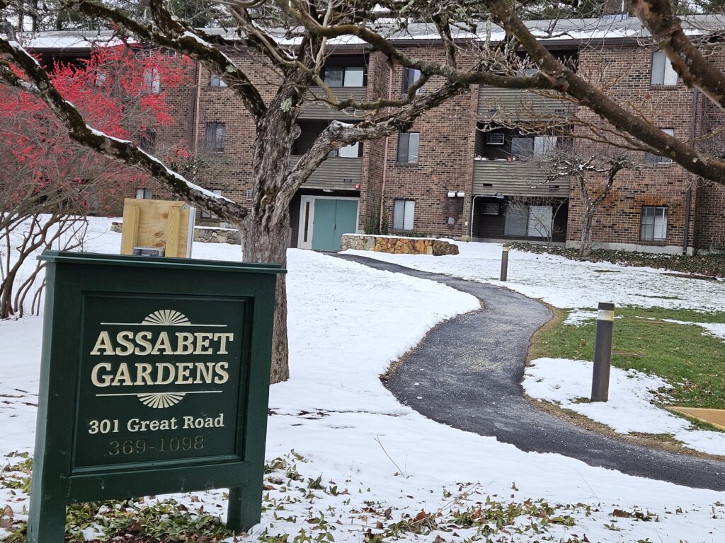 The green Assabet Gardens sign in front of the apartment buildings.