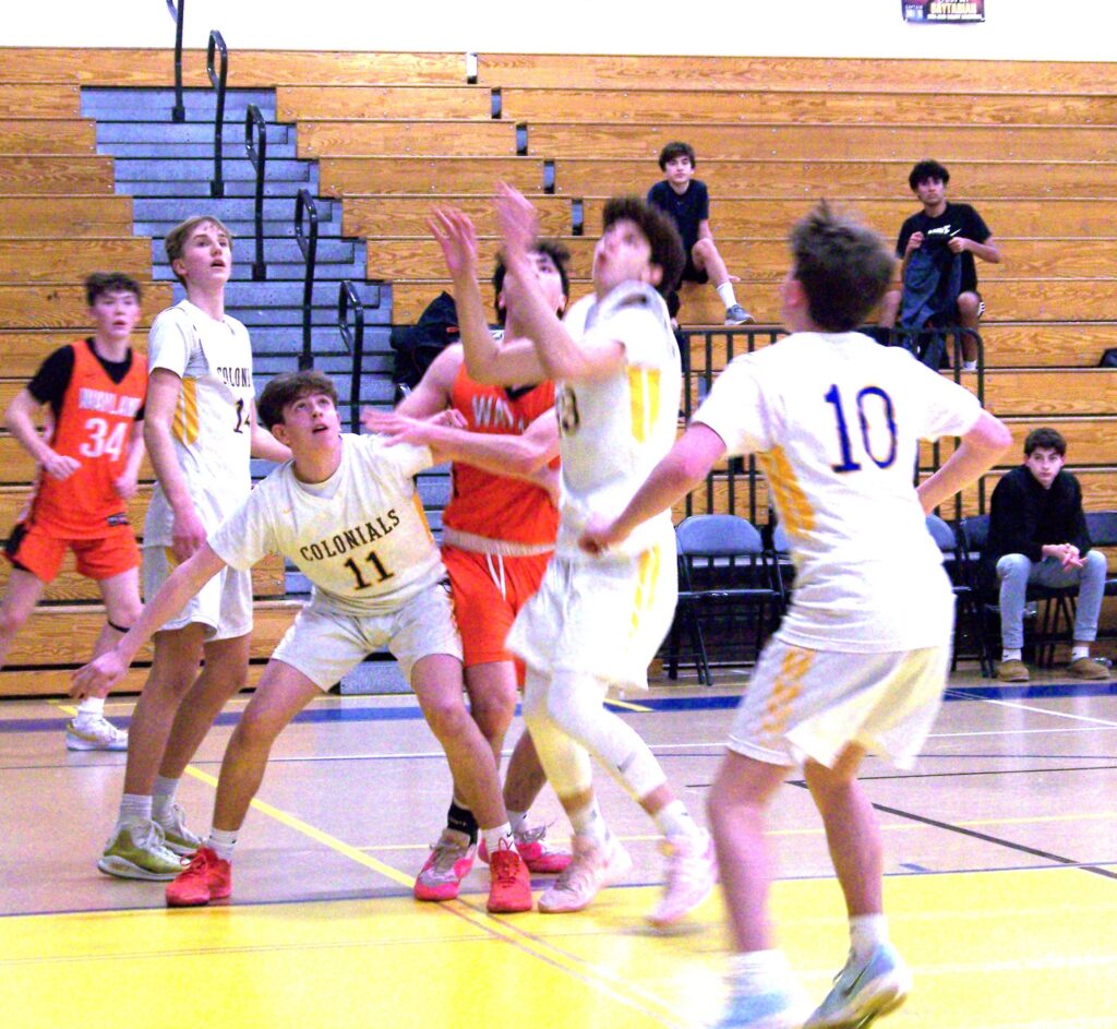 Players in both white (AB) and orange (Wayland) wait for a ball to come down from above.