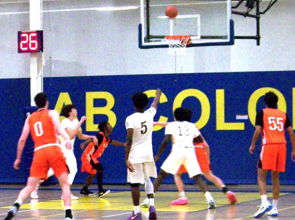 A bunch of boys in front of the basket. The ball is just about to go in and AB player 5 has is arm in the air (from just making the shot).