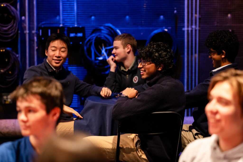 A group of young men sit at a table in a room with blue lights in the background.