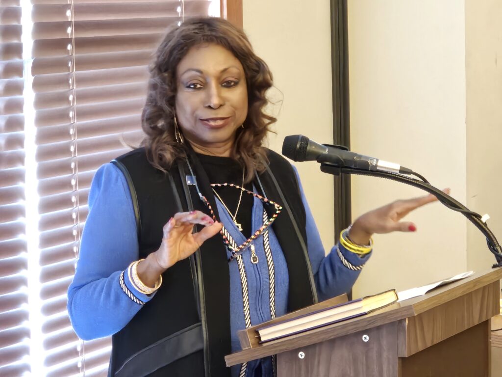 A woman wearing a blue sweater speaks as a podium.