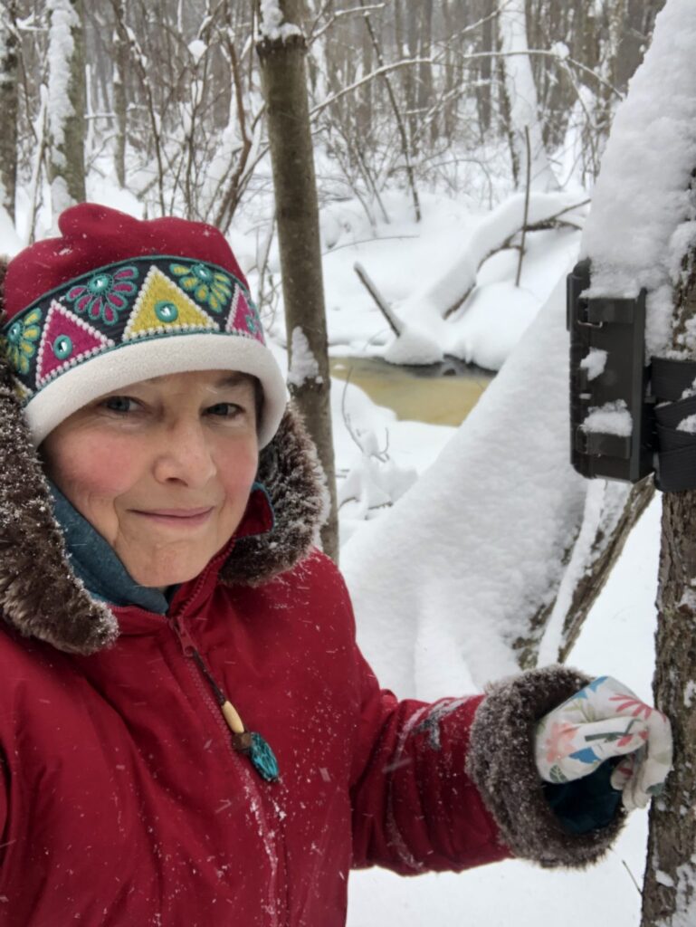 A woman out on a snowy day is bundled up against the cold in a red parka and embroidered red hat. She's wearing thin gloves, probably so she can check on her cameras.