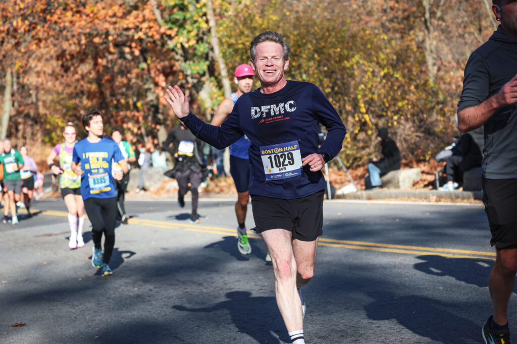 A man runs on a bright fall day. He's happy enough that he can smile and wave.