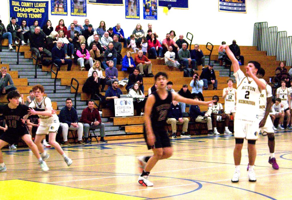 A group of basketball players on the court. One, wearing AB whites, stands with his arm straight out after throwing the ball.