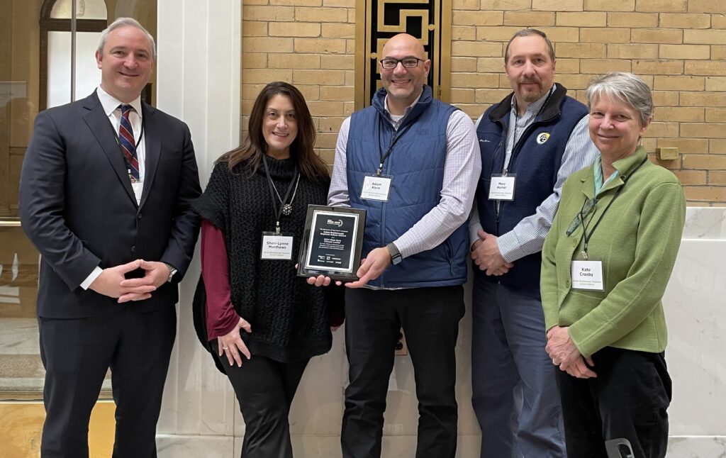 A man holding a plaque is flanked by other people.