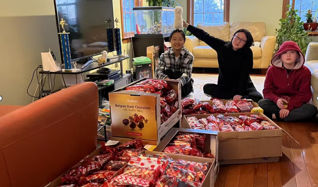 Three people sit on the floor with many boxes of candy.