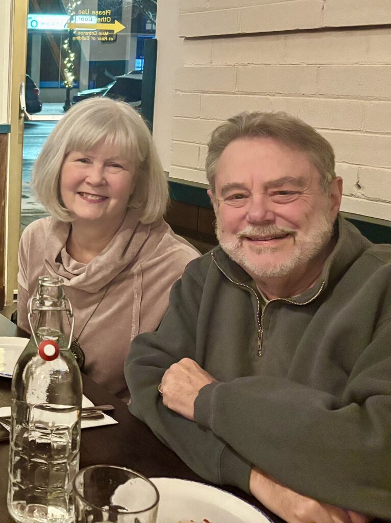 An older, smiling, couple sit at a restaurant table.