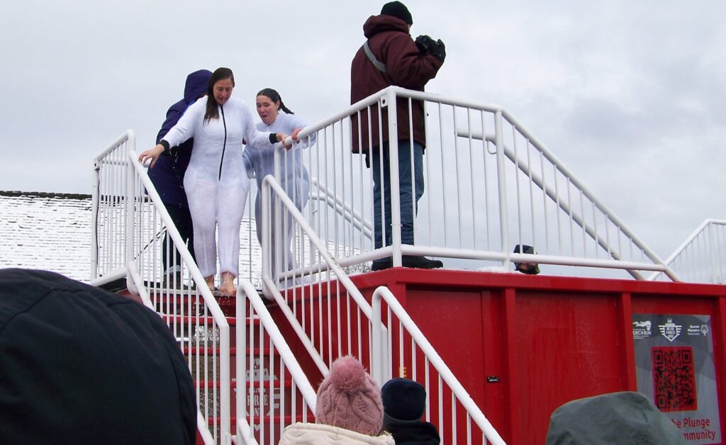 Two wet women in white onesies are climbing down the steps from the dunk tank. Hopefully someone's got towels for them.