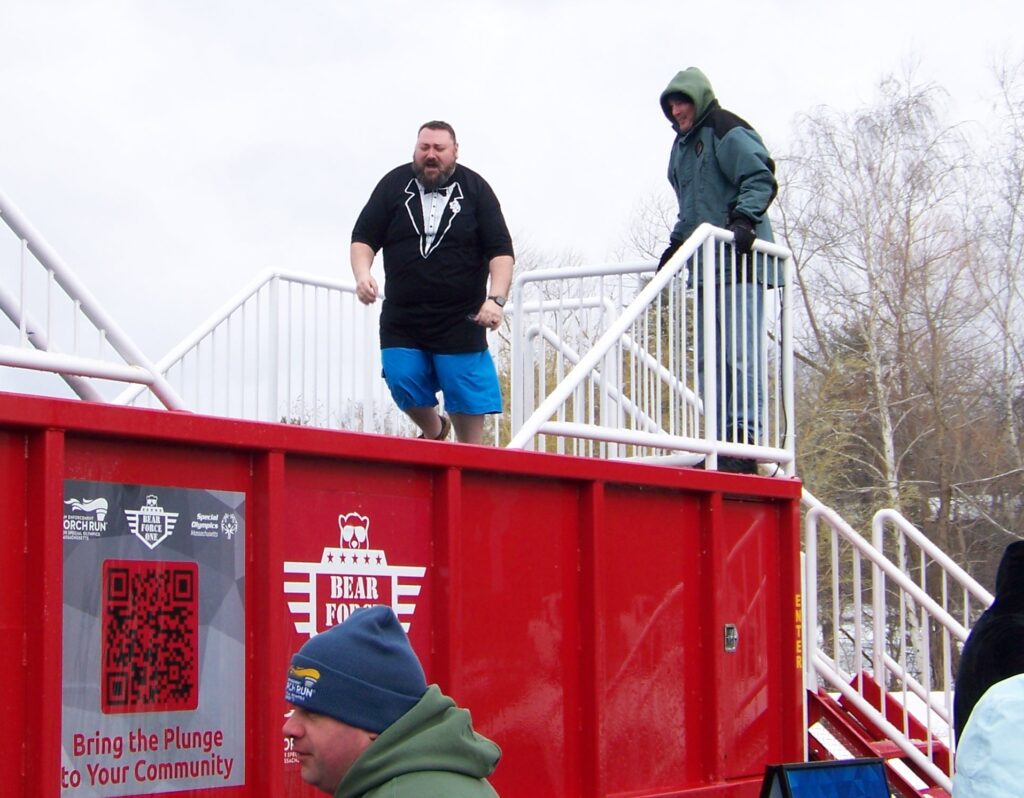 A large man wearing a tuxedo-printed T-shirt jumps into the tank.