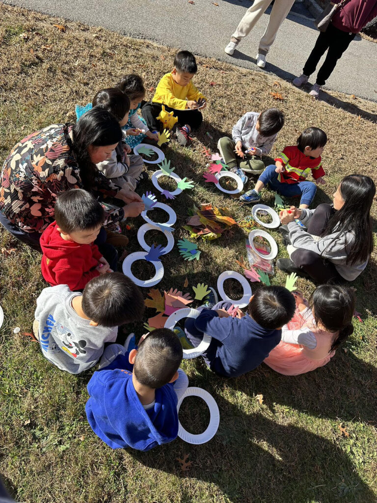 A group of young kids on a lawn doing a craft with paper plates.