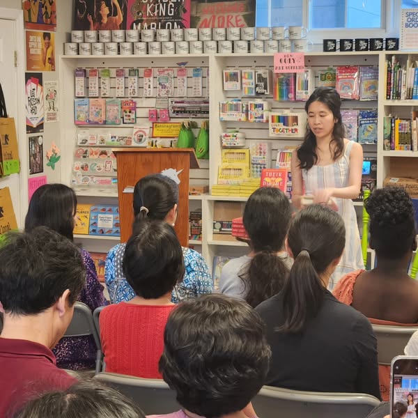 A woman holding a books speaks to a group of seated adults.