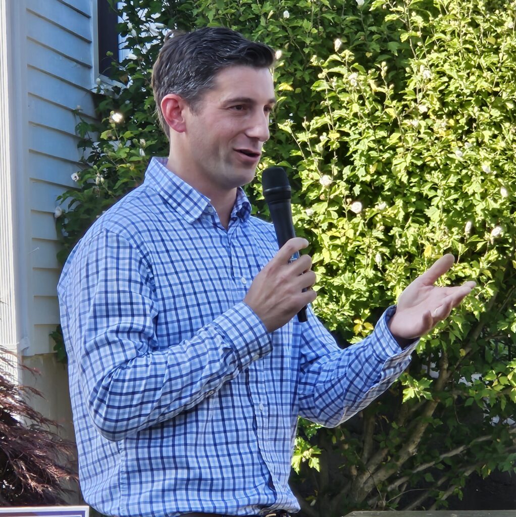 A man in a button-down shirt speaks into a mic.