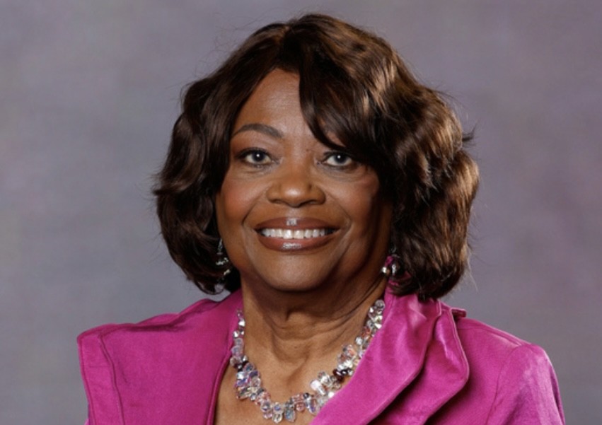 A smiling Black woman in a pink dress and sparkly necklace.