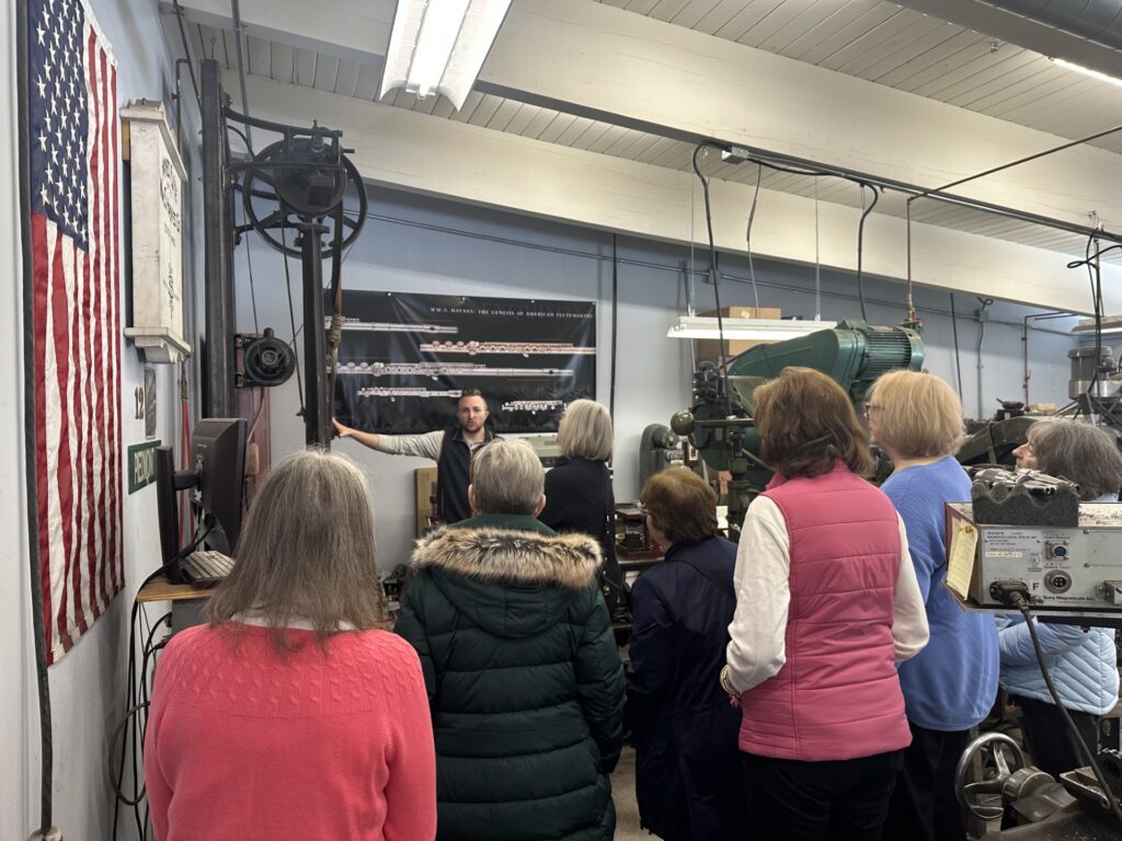 A man points to a machine hanging on a wall. A group of women gather around him listening.