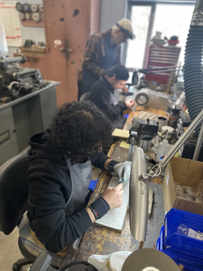 Three people sit or stand at workbenches full of tools.