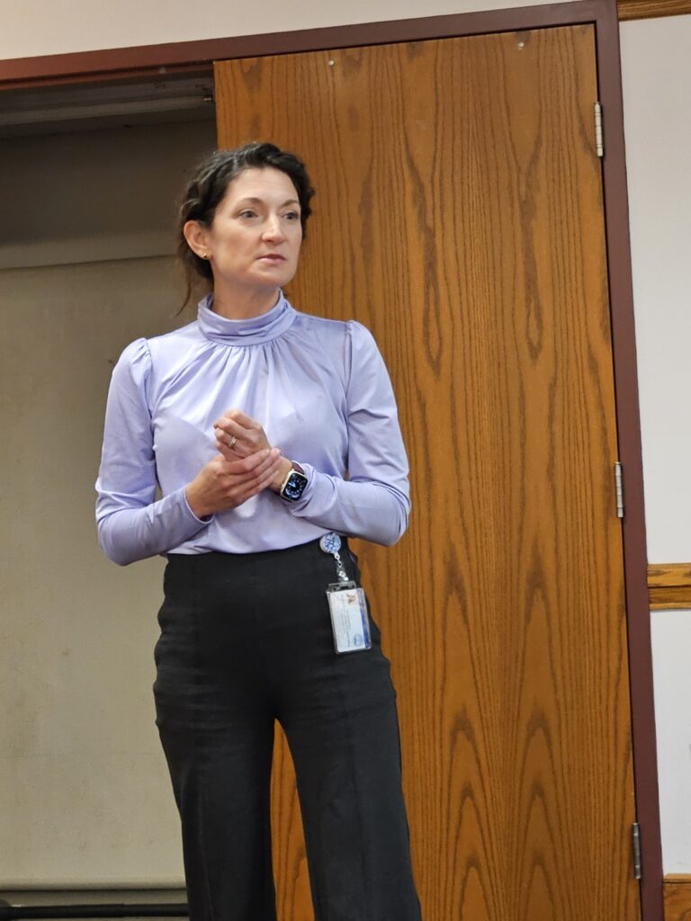 A woman in a purple shirt stands in front of a wooden door.