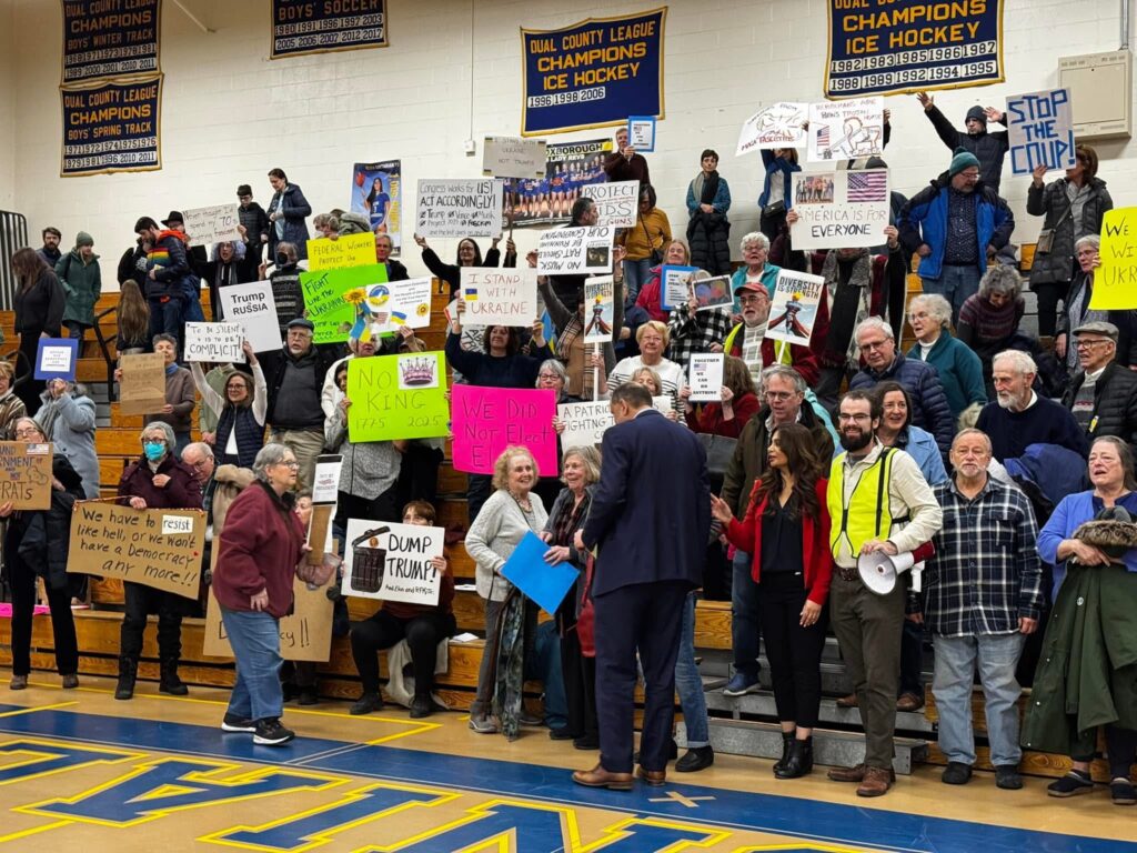 Full bleachers at the high school gym. Many people are holding signs.